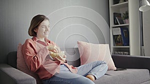 Young happy woman sitting on the sofa and watching camedy movie on TV