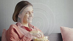 Young happy woman sitting on the sofa and watching camedy movie on TV