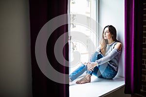 Young happy woman sitting on a window-sill at home and looking outside