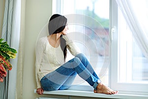 Young happy woman sitting on a window-sill