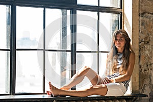 Young happy woman sitting on a window-sill and looking outside