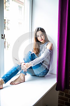 Young happy woman sitting on a window-sill at home and looking outside