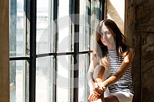 Young happy woman sitting on a window-sill and looking outside