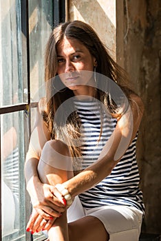 Young happy woman sitting on a window-sill and looking outside