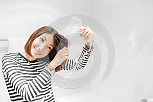 Happy woman smiling and drying her hair with hairdryer near the mirror in the bathroom