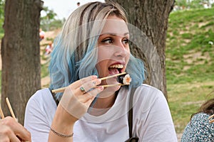 Young happy woman smiling and eating sushi in a park