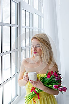 Young happy woman smiling with tulip bunch and cup tea. 8 march