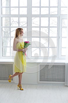 Young happy woman smiling with tulip bunch in yellow dress.