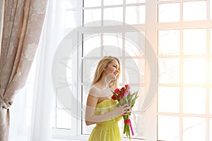 Young happy woman smiling with tulip bunch in yellow dress, sunlight