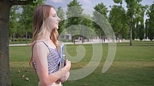 Young happy woman student walks in the park with a notebook and textbook