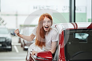 Young happy woman surprised by a new car at car showroom, gift from her husband