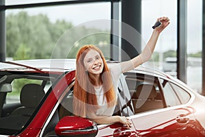 Young happy woman surprised by a new car at car showroom, gift from her husband