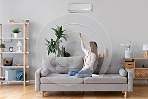 Young woman switching on air conditioner sitting on couch photo