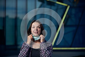 Happy woman takes off protective medical mask outdoors against modern city background. Pandemic Covid-19 is over photo