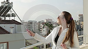 Young happy woman taking self portrait standing on the roof of the house using smartphone mobile cell phone camera