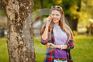 Young happy woman talking on cell phone in summer city park. Beautiful modern girl in sunglasses with a smartphone, outdoor