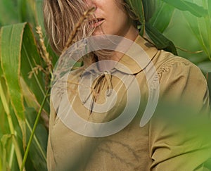 Young beautiful elegant girl in green corn field holding the stalks with her hands