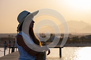 Young happy woman tourist relaxing outdoors on warm sunny evening on sea shore. Summer vacations and travelling concept