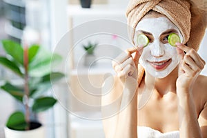 Young happy woman in towel, applying facial clay Mask in stylish bathroom.