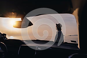 Young happy woman traveler enjoying sunset on sea beach, shot through car window