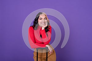 Young happy woman traveler with suitcase against purple background