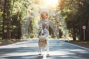 Young happy woman with traveling backpack wearing hat stand alone on countryroad