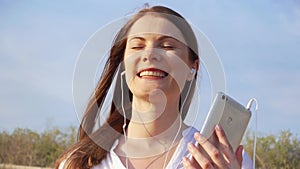 Young happy woman using mobile against blue sky. Female listening music via cellphone in slow motion