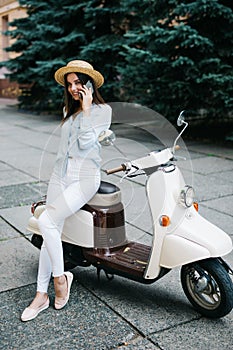 Young happy woman using mobile phone on moped