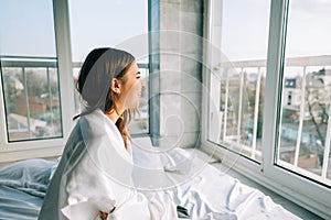 Young happy woman wake up in the morning, sitting on bed and looking on window