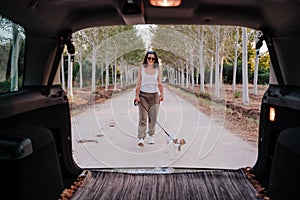 Young happy woman walking outdoors with her dog. Travel concept. View from inside the car