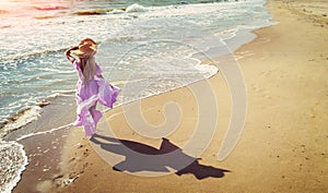 A young happy woman walks carelessly along the seashore in a pink flowing