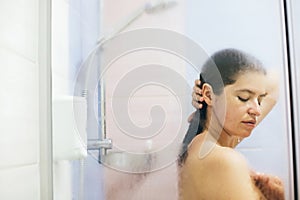 Young happy woman washing her hair, washing away shampoo foam. Portrait of beautiful brunette girl taking shower and enjoying time