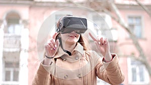 Young happy woman wearing cyberspace virtual reality headset glasses having fun outside on street in beige outwear coat