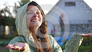 Young happy woman wearing raincoat is feeling free and smiling under the rain. Concept of life, freedom, nature