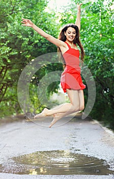 Young happy woman wearing red dress jumping into a puddle