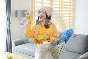 Young happy woman wearing yellow gloves  and holding a basket of cleaning supplies in living room