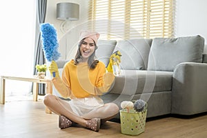 Young happy woman wearing yellow gloves  and holding a basket of cleaning supplies in living room