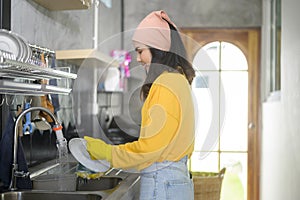 Young happy woman wearing yellow gloves washing dishes in kitchen at home