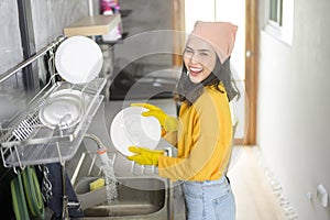 Young happy woman wearing yellow gloves washing dishes in kitchen at home