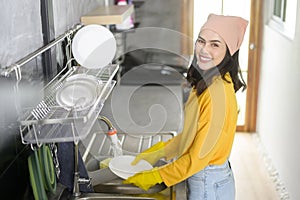 Young happy woman wearing yellow gloves washing dishes in kitchen at home