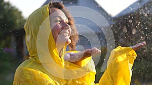 Young happy woman wearing yellow raincoat is feeling free and smiling under the rain. Concept of life, freedom, nature