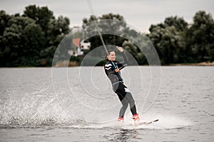 Young happy woman in wetsuit holds rope with her hand and rides the wave on wakeboard