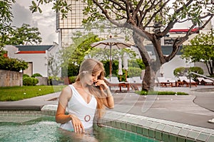 Young happy woman in white swimwear relax in swimming pool in modern tropical resort. Luxury vacation, Asia trip