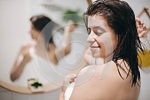 Young happy woman in white towel enjoying spa and wellness, relaxing in bathroom with mirror. Hair and body care. Slim woman