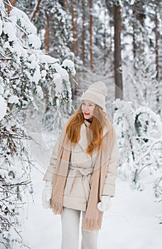 Young happy woman in winter clothes walks in the snowy forest