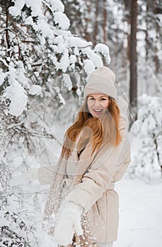 Young happy woman in winter clothes walks in the snowy forest