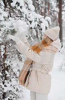 Young happy woman in winter clothes walks in the snowy forest