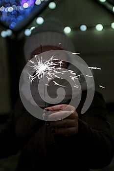 young happy woman in a winter hat holds a sparkler in front of her