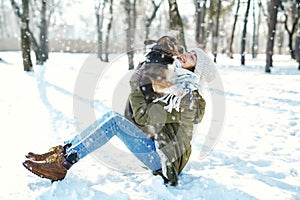 Young happy woman in woolen hat and long warm scarf holding her pet in snowy winter park at frozzy sunny day