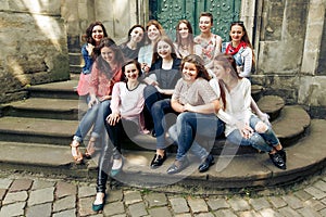 Young happy women sitting on stairs posing on background of old european city street, stylish hipster girls, moments of happiness